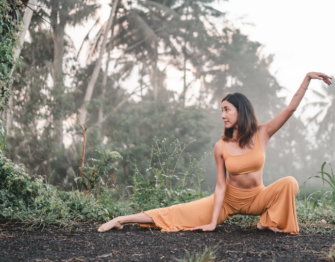 Woman in a yellow outfit performing a yoga pose in a forest setting