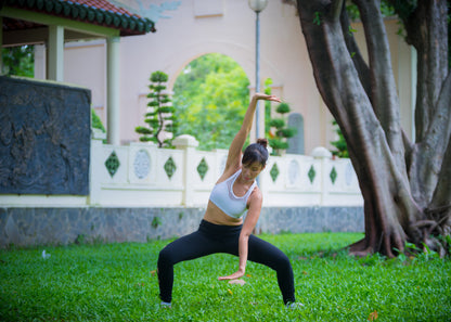 Woman practicing yoga in a park with trees and a building in the background
