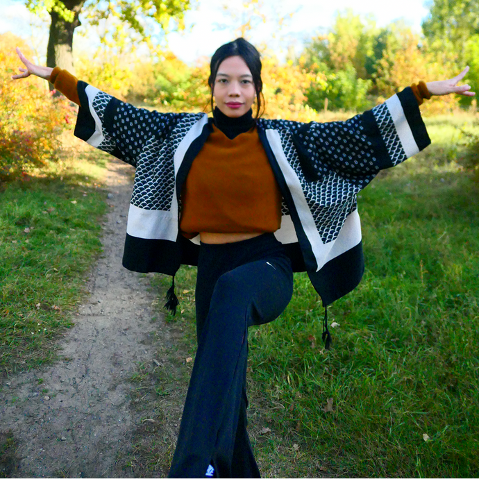 Person standing outdoors with arms outstretched, surrounded by trees with autumn foliage.