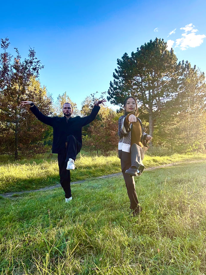 Two people posing outdoors in a grassy area with trees and blue sky.