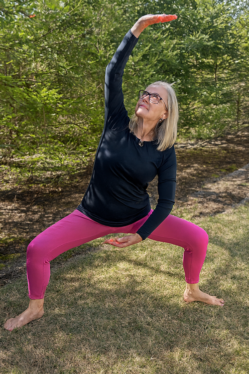 Woman in pink leggings and black top performing a Qigong-yoga pose outdoors.