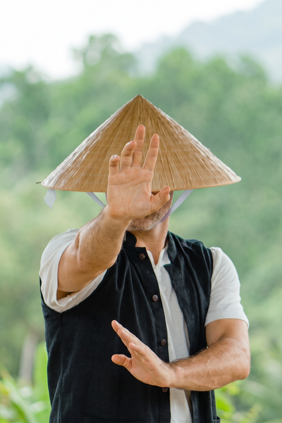 Tevia Feng in a conical hat, one hand raised in a qigong form